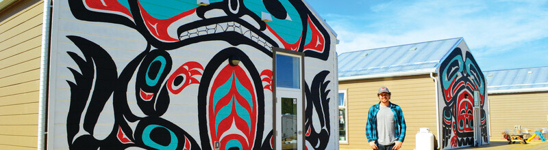 Un étudiant au programme co-op pose pour une photo près d'une murale d'art indigène à Whitehorse, Yukon