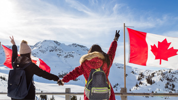 Deux jeunes femmes se tenant la main à côté de drapeaux canadiens dans les montagnes de Whistler en Colombie-Britannique