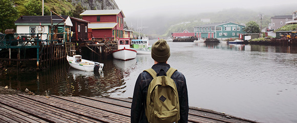 Góc nhìn từ phía sau của sinh viên đeo ba lô đang chiêm ngưỡng một làng chài nhỏ ở Newfoundland